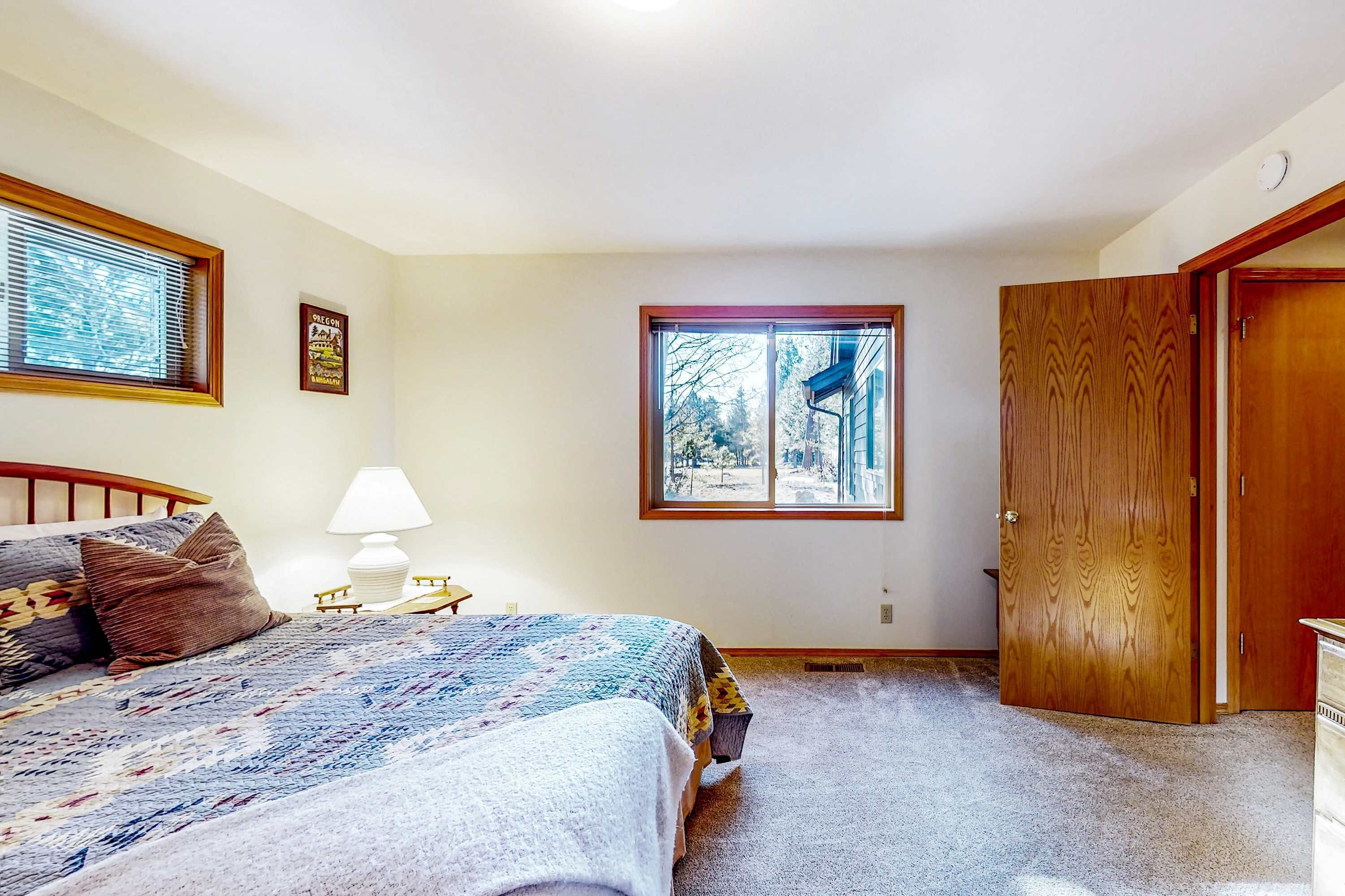 A bedroom with a bed, a nightstand, a lamp, a window, and a door.