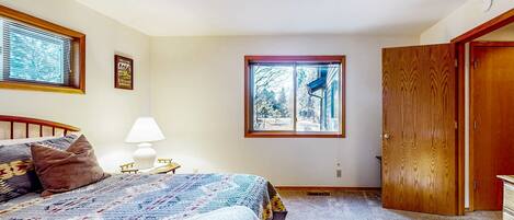 A bedroom with a bed, a nightstand, a lamp, a window, and a door.