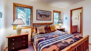 A bedroom with a bed, two nightstands, a lamp, a painting, and a window. - Spacious home with fireplace, private hot tub, AC, & SHARC passes (Sunriver)