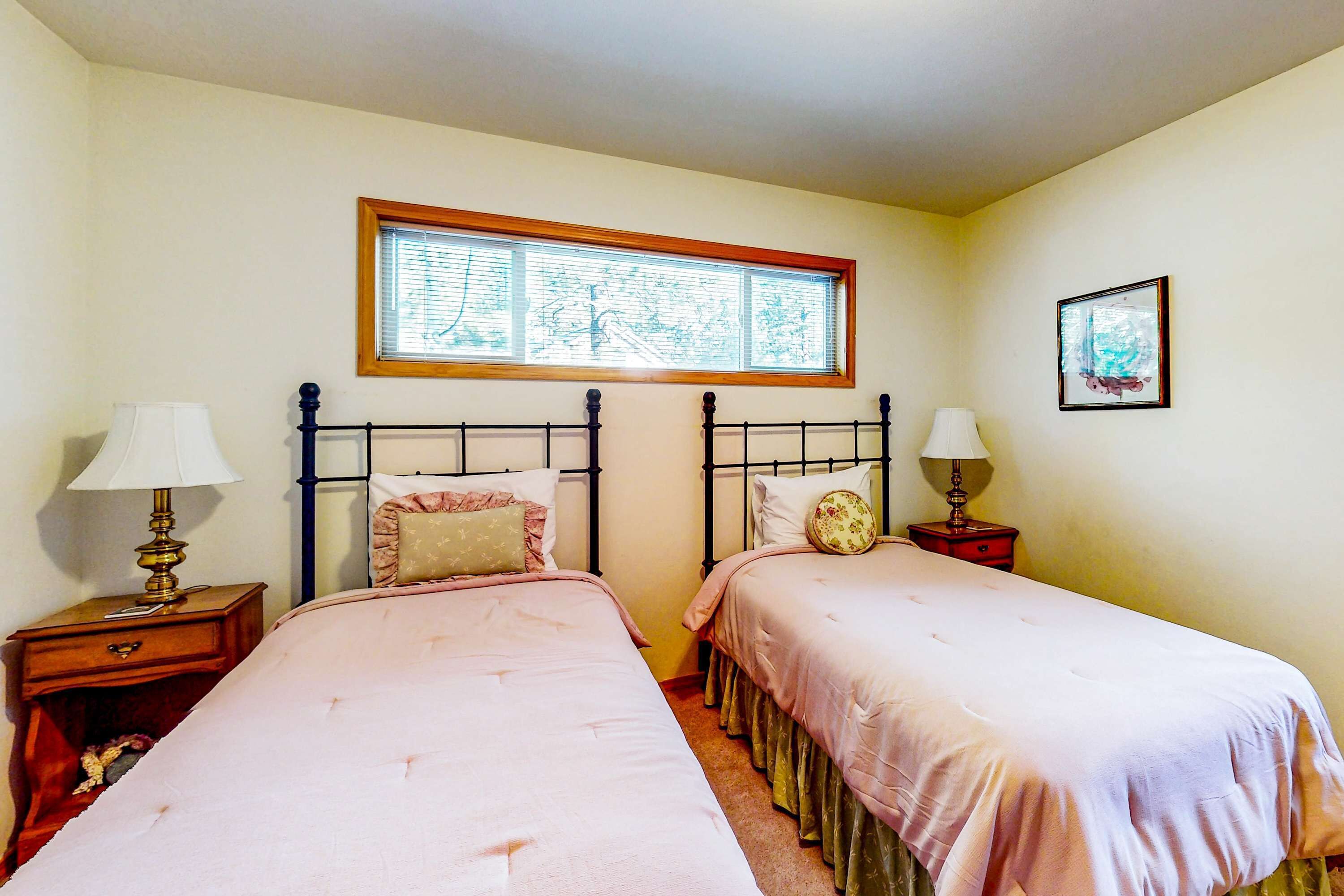 A bedroom with two beds, a window, and a framed picture on the wall.