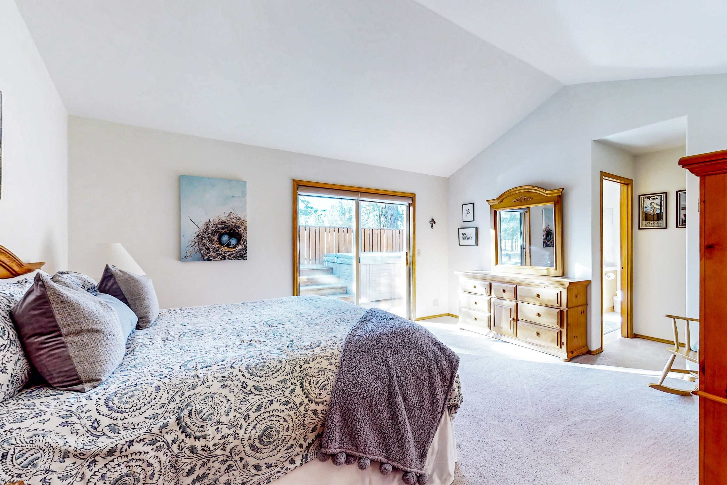 A bedroom with a large bed, a dresser, a mirror, and a door leading to a balcony.