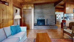 A wooden interior with a fireplace, a sofa, a chair, and a kitchen area. - Unique lakefront cabin near the dunes with a private dock & fireplace (Florence)