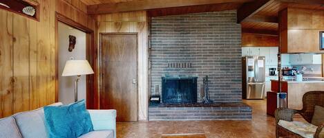 A wooden interior with a fireplace, a sofa, a chair, and a kitchen area.