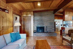 Un interior de madera con chimenea, un sofá, una silla y una zona de cocina.