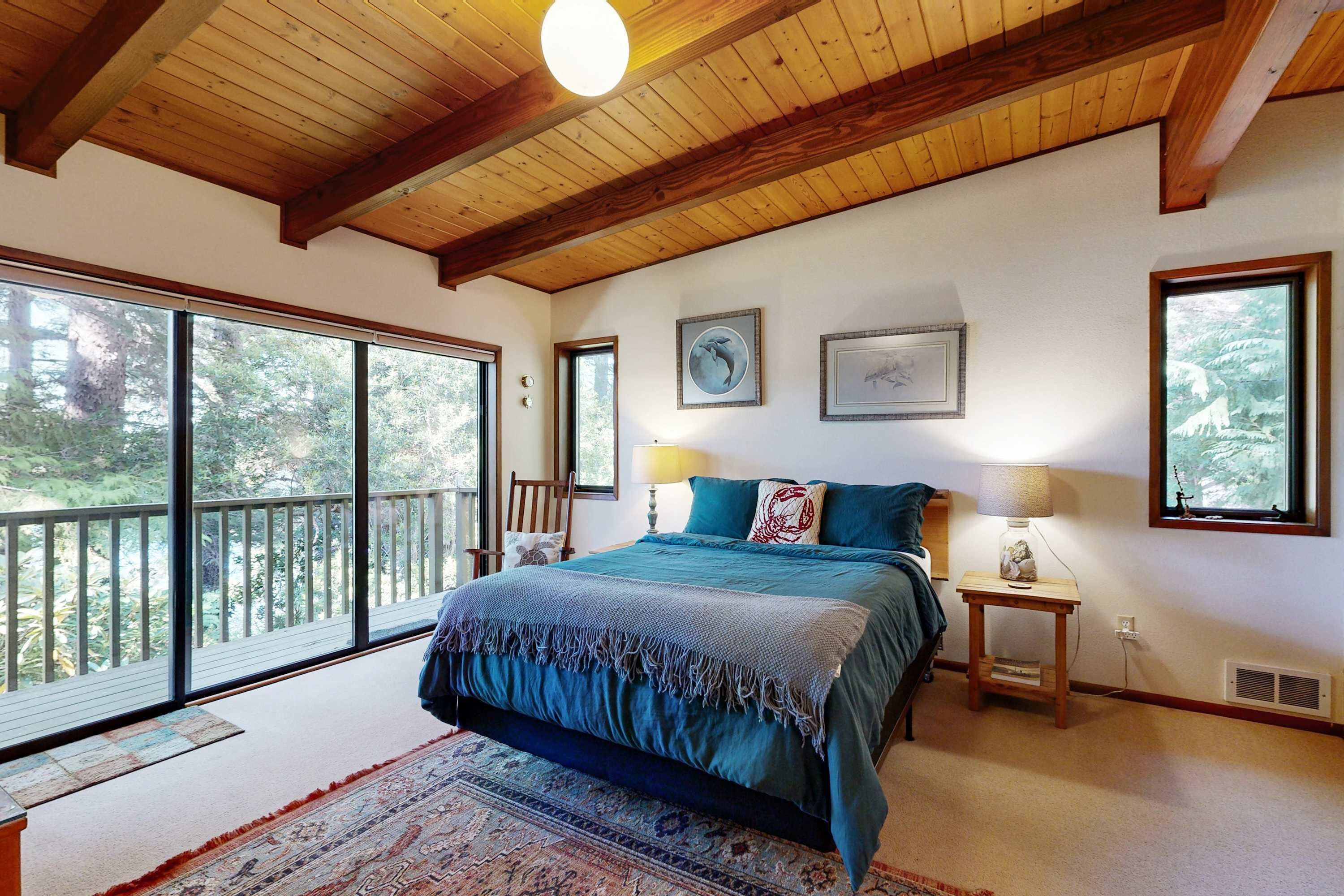Un dormitorio con una cama grande, techo de madera, vistas amplias por grandes ventanales y una mesita de noche pequeña.
