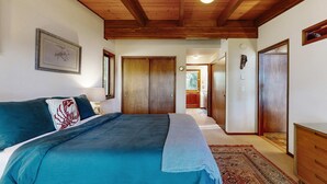 A bedroom with a bed, wooden ceiling, a framed picture, a door, and a hallway leading to a bathroom. - Unique lakefront cabin near the dunes with a private dock & fireplace (Florence)