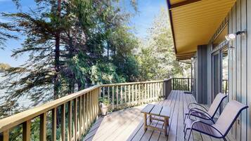 Une terrasse en bois avec une rambarde, une table et des chaises, d’où l’on peut admirer un plan d’eau et des arbres.
