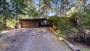 A gravel driveway leading to a wooden garage, surrounded by dense forest and tall trees. - Unique lakefront cabin near the dunes with a private dock & fireplace (Florence)