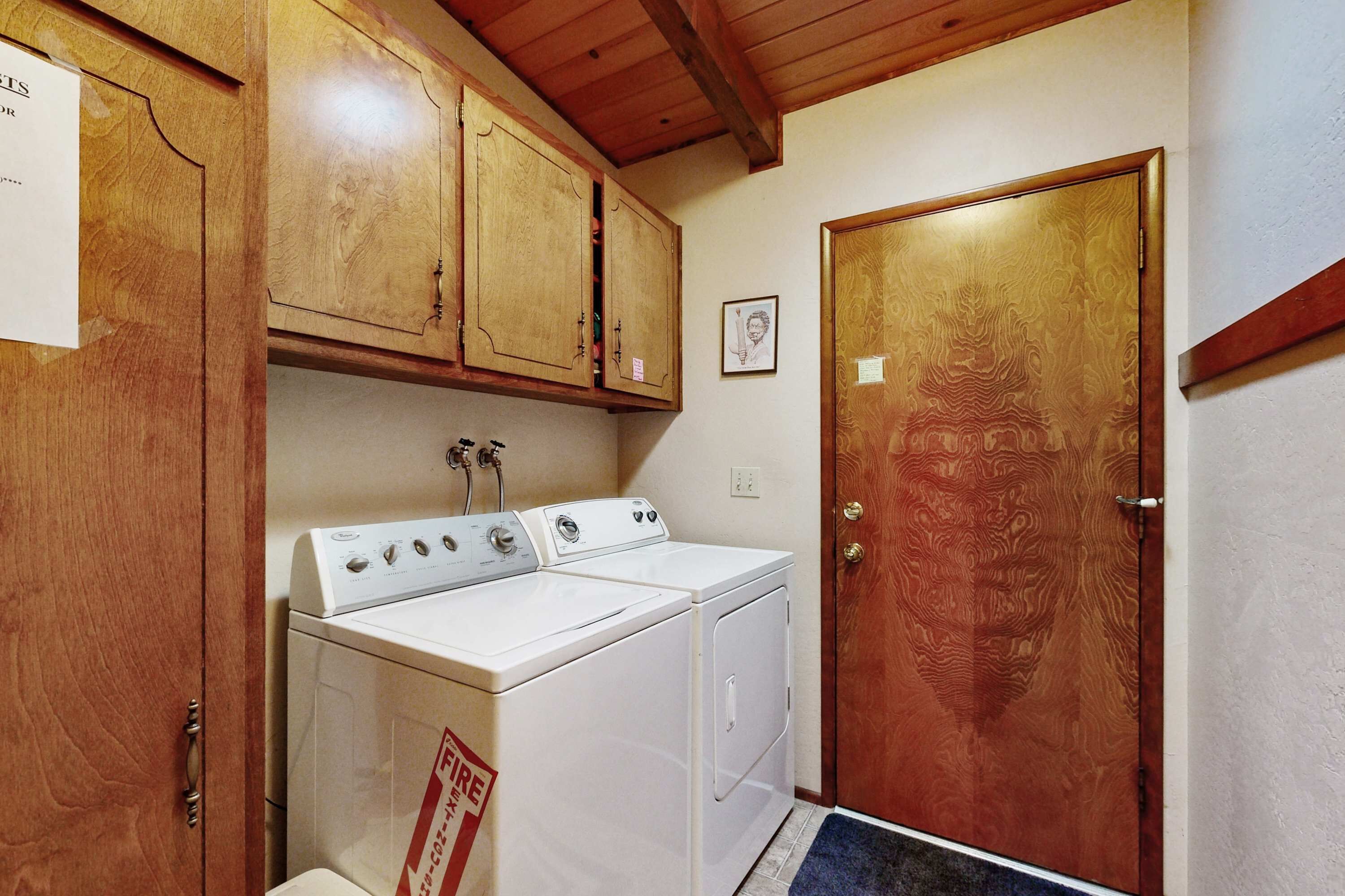 A laundry room with wooden cabinets, a white washer and dryer, and a wooden door.