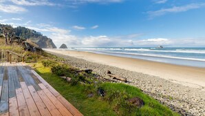 Una pasarela de madera que lleva a una playa de piedras con vista al océano a lo lejos.