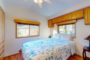 A bedroom with a bed, wooden cabinets, a ceiling fan, and windows with blinds.