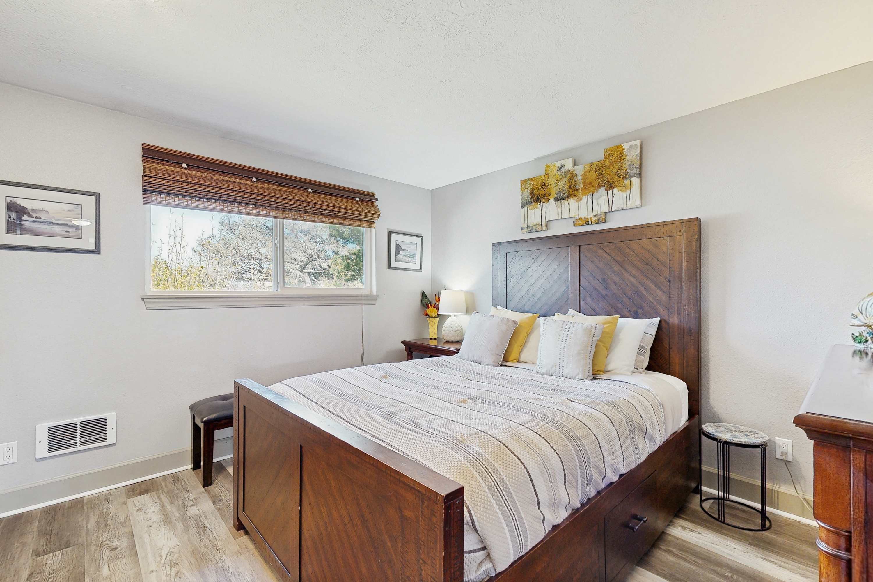Une chambre à coucher avec un grand lit, une table de chevet, une commode, une fenêtre avec des stores et une œuvre d’art accrochée au mur.