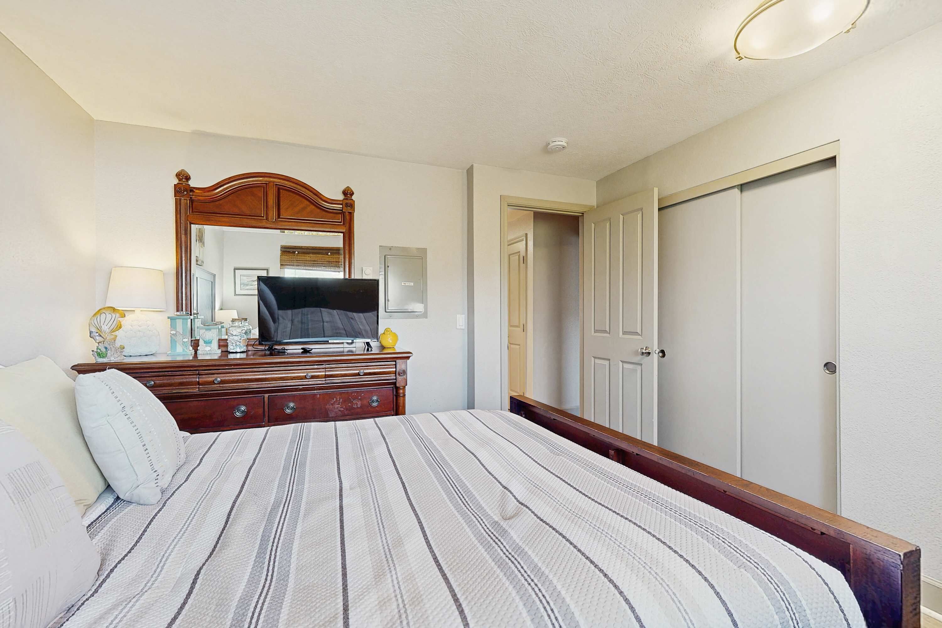 A bedroom with a bed, dresser, television, and a door.