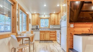 A kitchen with wooden cabinets, a dining table with chairs, and a refrigerator. - Dog-friendly cabin with deck, fenced yard, game room, & hot tub (Rhododendron)