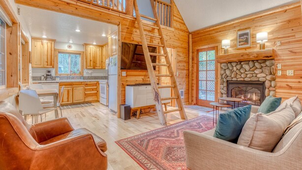 A log cabin interior with a kitchen, dining area, and a fireplace. - Dog-friendly cabin with deck, fenced yard, game room, & hot tub (Rhododendron)