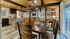 A spacious dining area with a wooden table and chairs, a kitchen in the background, and a large window providing natural light. - Remodeled home with hot tub, SHARC passes, & close to Sunriver Village - dogs OK (Sunriver)