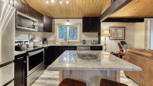 A modern kitchen with stainless steel appliances, a wooden ceiling, and a large island with stools. - Remodeled home with hot tub, SHARC passes, & close to Sunriver Village - dogs OK (Sunriver)