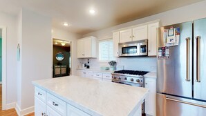 A kitchen with white cabinets, a stainless steel refrigerator, a microwave, and a stove. - Coastal beach retreat with deck, grill, fireplace, washer&dryer, and free WiFi (Seaside)