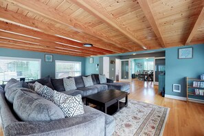 A spacious living room with a large sectional sofa, a dark coffee table, and a wooden ceiling. - Coastal beach retreat with deck, grill, fireplace, washer&dryer, and free WiFi (Seaside)