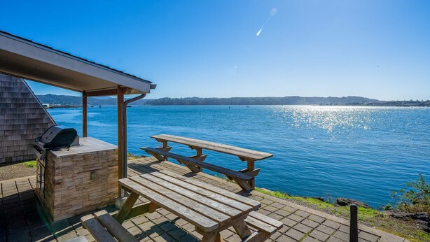 Ein Holztisch mit Grill am See unter blauem Himmel.