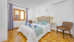 Une chambre à coucher comprenant un lit, deux tables de chevet, une chaise, une fenêtre avec des rideaux et un appareil de climatisation.