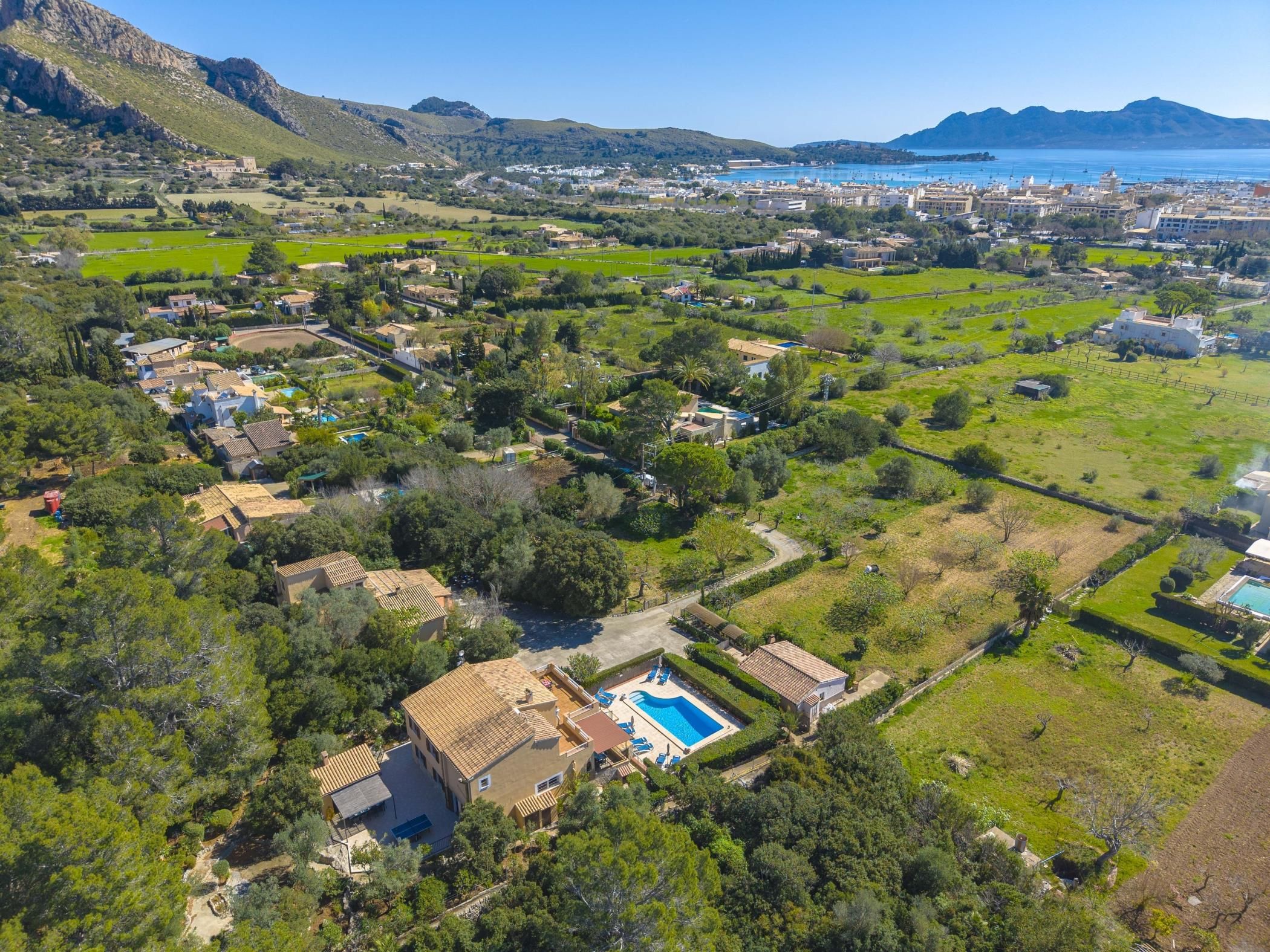 An aerial view of a residential area with houses, green fields, and a swimming pool.