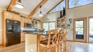 A kitchen with wooden cabinets, a black refrigerator, a wooden island with bar stools, and large windows. - Home near Deschutes River, WiFi, & private hot tub - dogs ok (Sunriver)