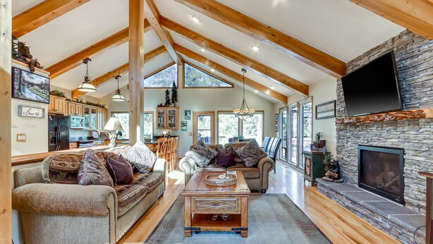 A spacious living area with wooden beams, a stone fireplace, and a large TV mounted on the wall. - Home near Deschutes River, WiFi, & private hot tub - dogs ok (Sunriver)