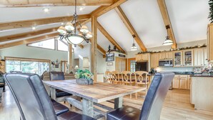 A spacious dining area with a wooden table and leather chairs, a kitchen with wooden cabinets, and a high ceiling with exposed beams. - Home near Deschutes River, WiFi, & private hot tub - dogs ok (Sunriver)