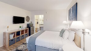 A modern hotel room with a bed, a TV, a console table, and a bathroom visible through an open door. - Cute beach room with fast WiFI - walk to downtown shops & eats (Bandon)