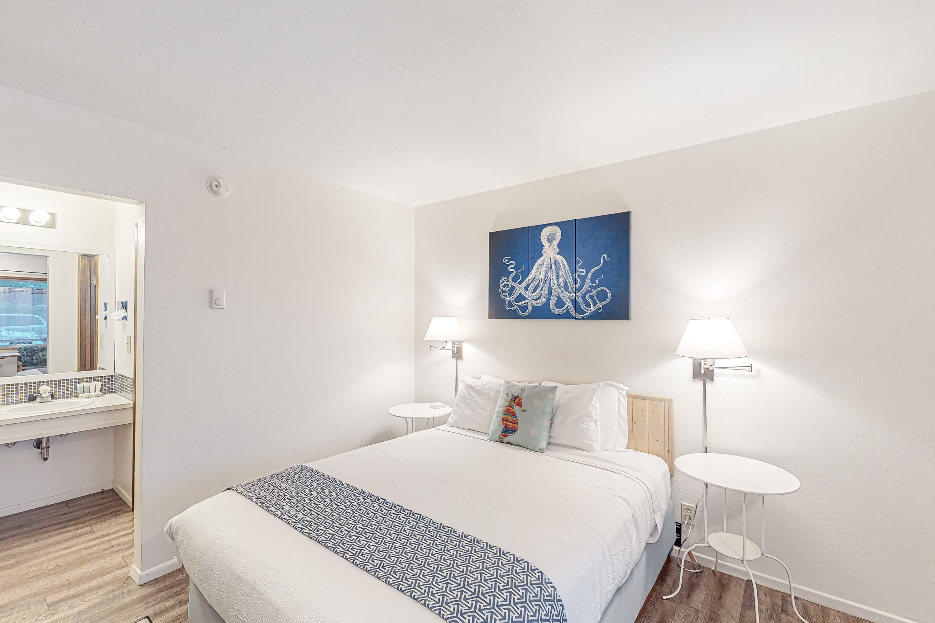 A hotel room with a bed, bedside tables, a large mirror, a painting, and a view of the pool.