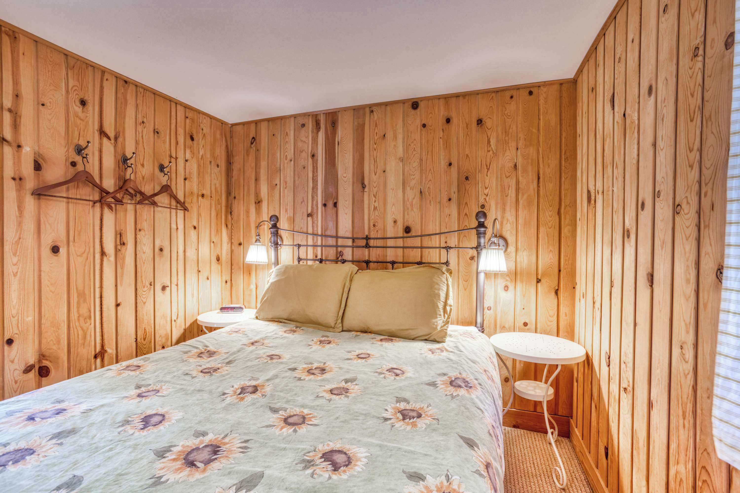 Une pièce aux murs lambrés, comprenant un lit, deux tables de chevet et un porte-manteau fixé au mur.