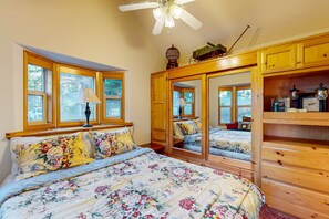 A bedroom with a large bed, wooden wardrobe, and a mirror cabinet. - Beautiful coastal cabin with private hot tub, gas grill & scenic deck space (Brookings)