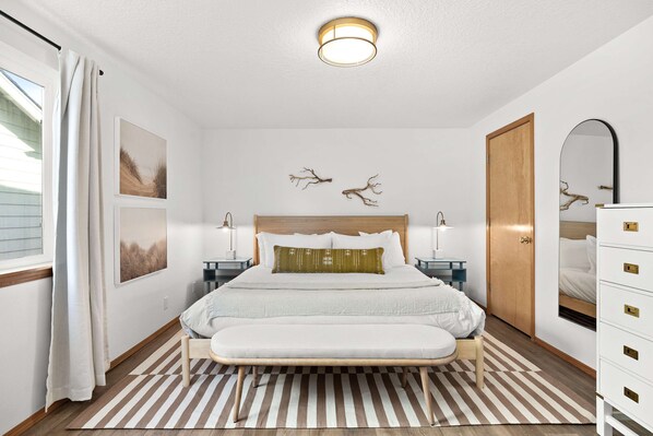 A bedroom with a bed, bedside tables, a mirror, and a wardrobe. - 1.5 blocks to beach & Prom - Charming home with private hot tub, deck, yard (Seaside)