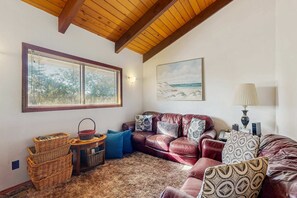 A cozy living room with a leather sofa, a patterned rug, wicker baskets, and a painting of a beach scene. - Dog-friendly home near the beach with large deck, yard & washer&dryer (Seaside)
