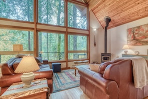Un intérieur de chalet chaleureux avec des canapés en cuir, une cheminée, de grandes fenêtres et un plafond en bois rustique.