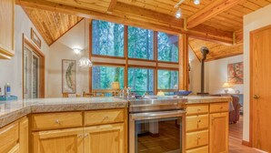 A kitchen with wooden cabinets, a stainless steel oven, and a large window with a view of trees.