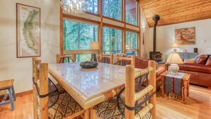 A wooden dining table with chairs, a map on the wall, and a large window with a forest view.