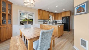 A kitchen with wooden cabinets, a dining table, chairs, a refrigerator, and a window with a view of a house. - Gorgeous dog-friendly home with spectacular ocean views & deck - walk to Main St (Manzanita)