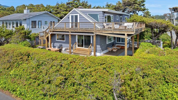 A two-story house with a deck, surrounded by dense greenery. - Gorgeous dog-friendly home with spectacular ocean views & deck - walk to Main St (Manzanita)