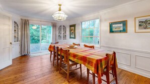 A dining room with a long table, wooden chairs, a chandelier, and large windows with curtains. - Oceanfront charmer with wood fireplace, games, & scenic deck - dog-friendly (Ocean Park)