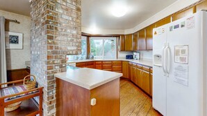 A kitchen with wooden cabinets, a brick accent wall, a refrigerator, and a window with a view. - Oceanfront charmer with wood fireplace, games, & scenic deck - dog-friendly (Ocean Park)