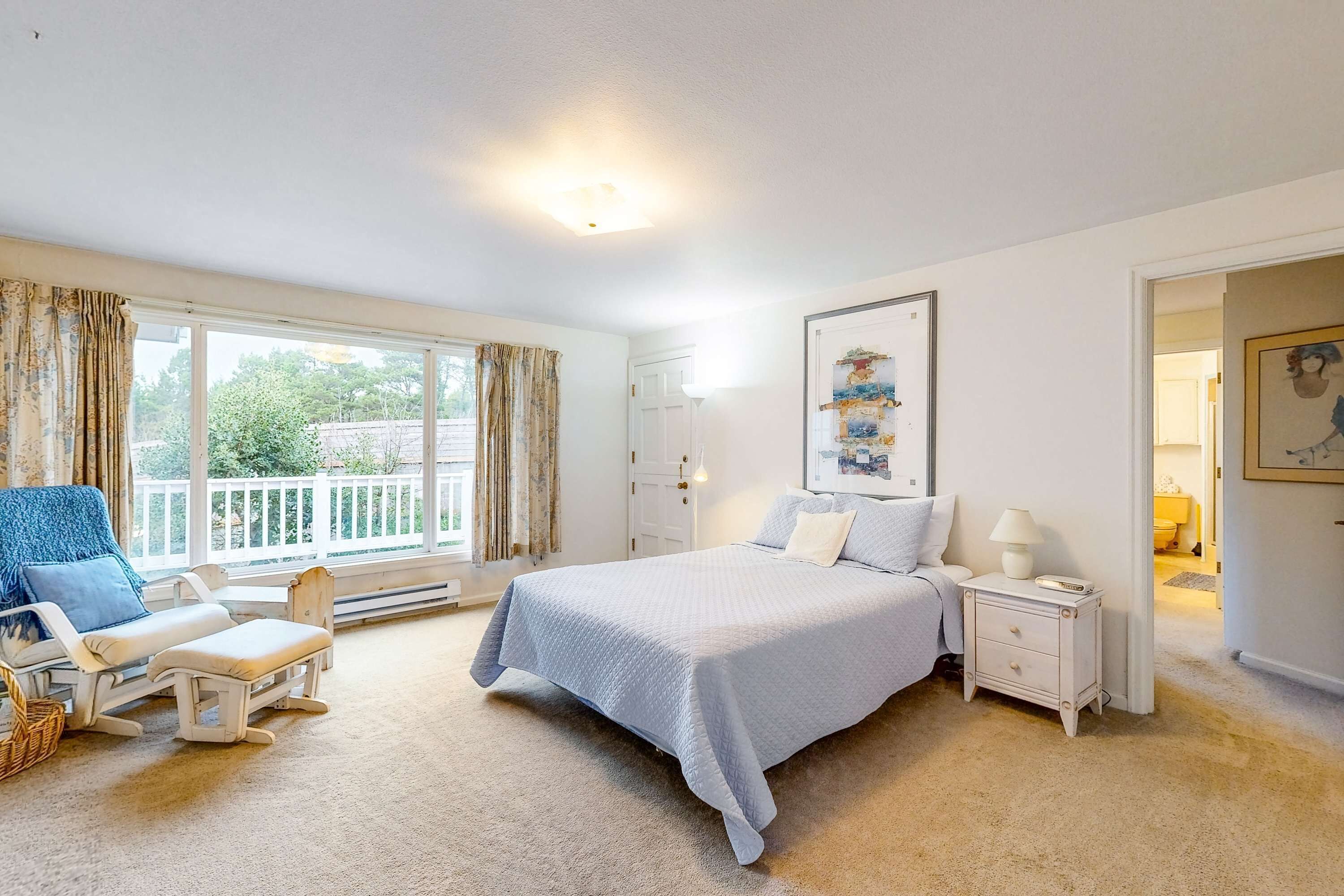 A bedroom with a bed, bedside tables, a chair, a window with curtains, and a door leading to another room.