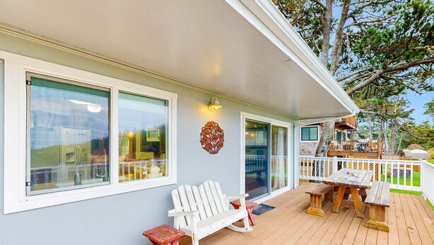 A covered deck with a wooden table and benches, a white Adirondack chair, and a railing. - Oceanfront charmer with wood fireplace, games, & scenic deck - dog-friendly (Ocean Park)