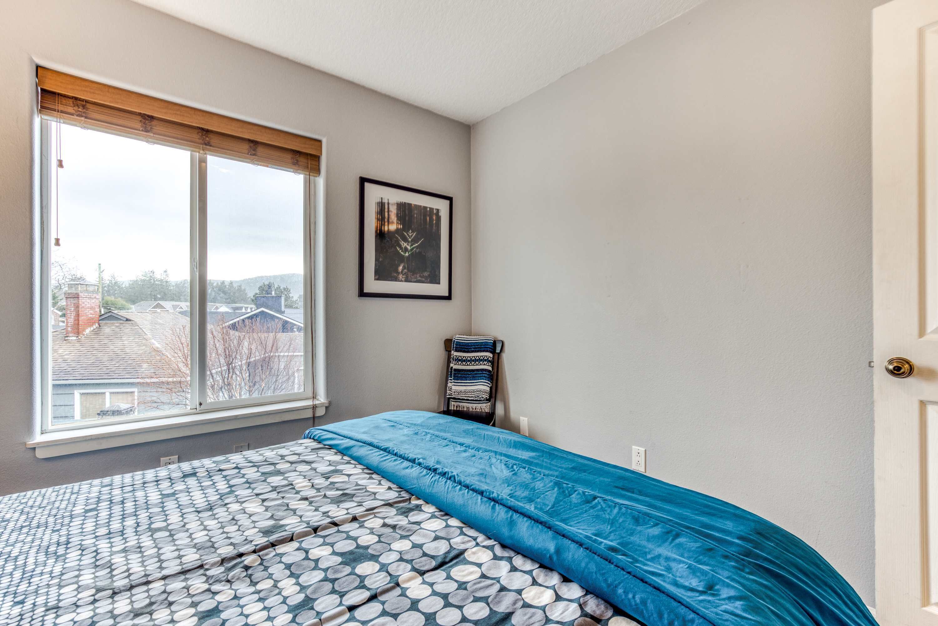 Ein Schlafzimmer mit einem Bett, einem Fenster, einem gerahmten Bild und einer Tür.