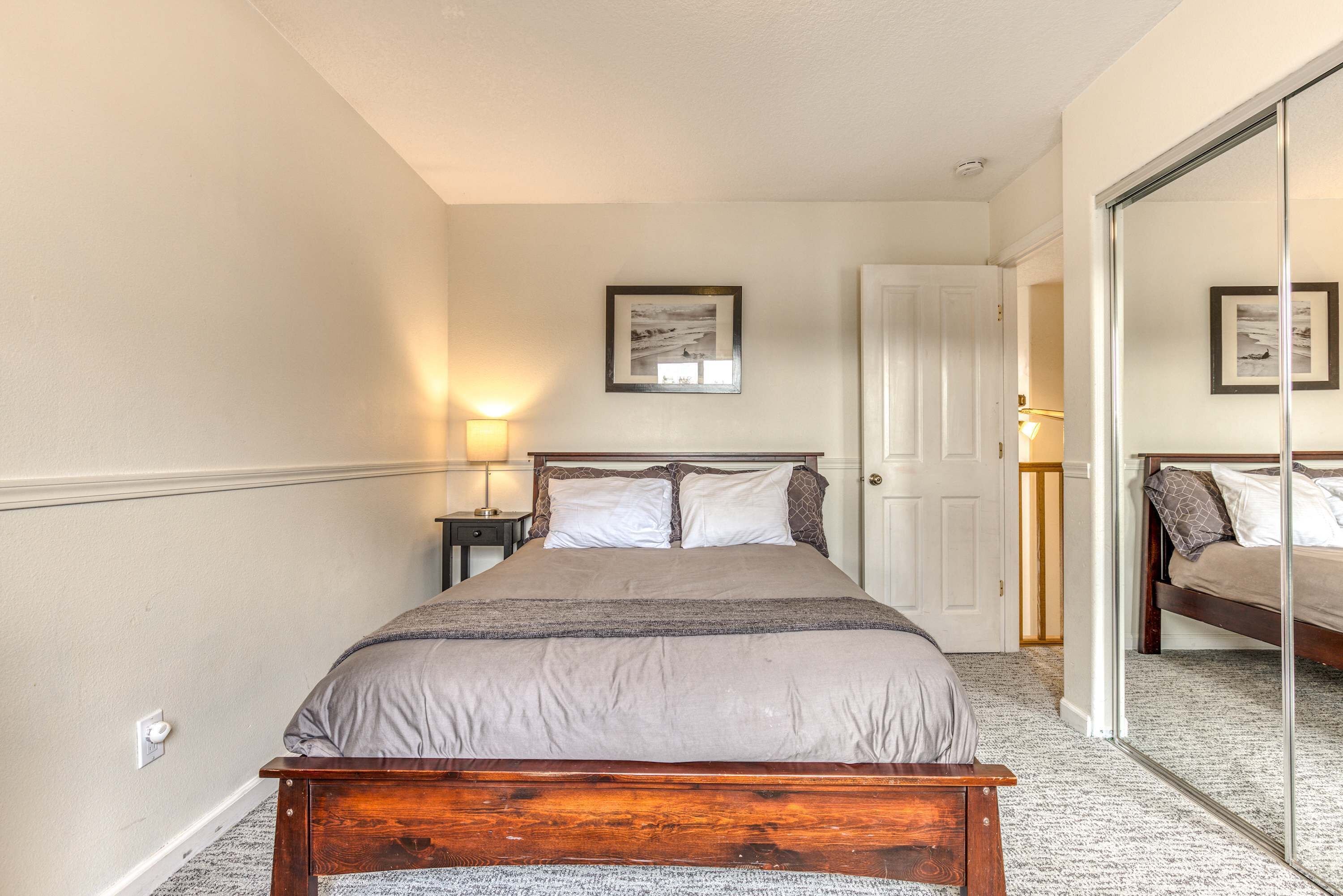 A bedroom with a bed, a bedside table, a lamp, a door, and a framed picture on the wall.