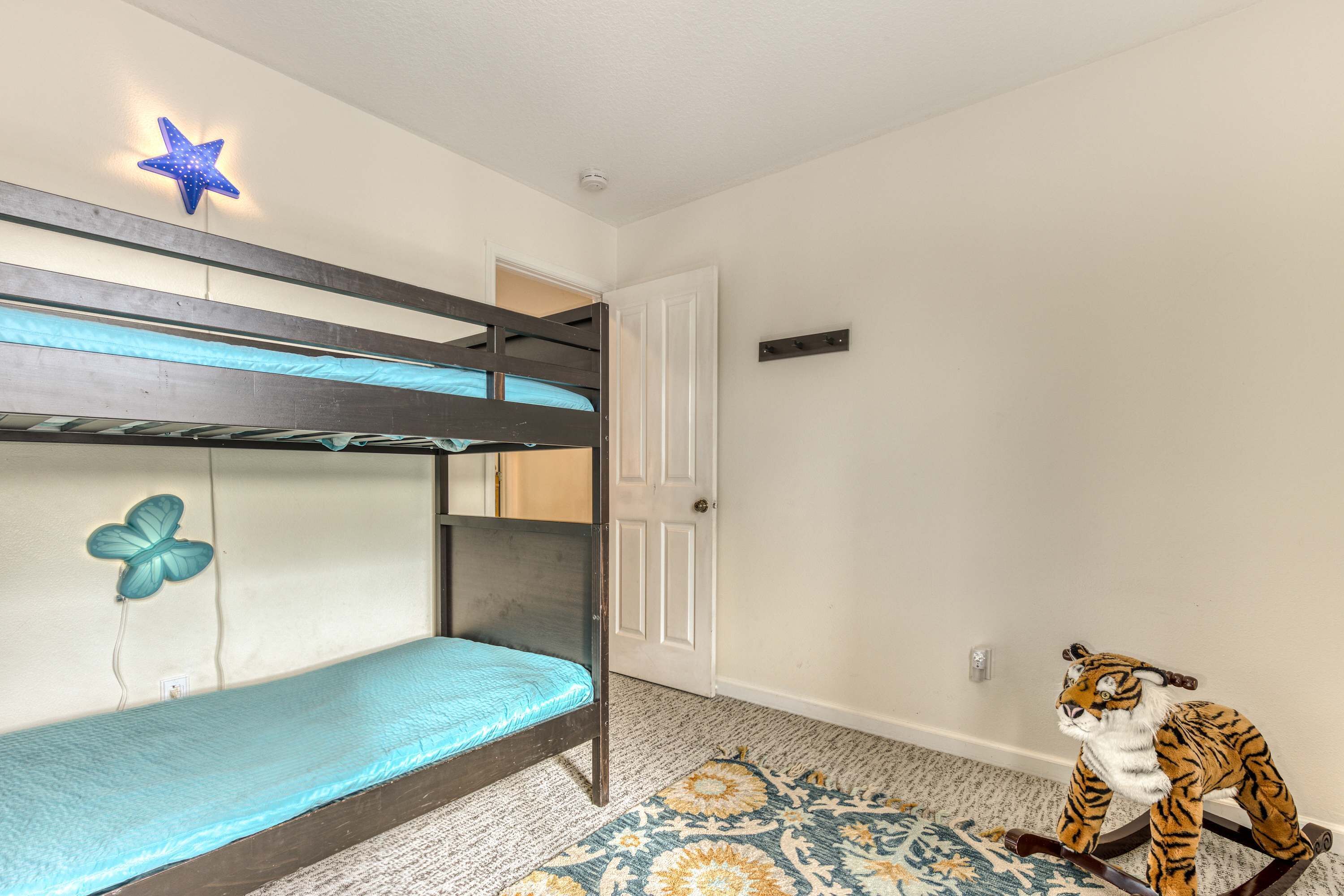 Un lit superposé décoré d’étoiles, un motif de papillon sur le mur et un jouet en forme de tigre posé sur le sol.