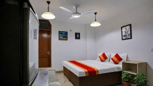 A bedroom with a bed, ceiling fan, two wall-mounted lights, a wooden door, and two potted plants. - Mauryan Elite I Hotel Hauzkhas  (New Delhi)