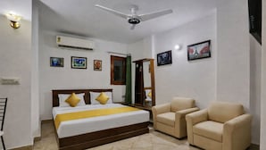A hotel room with a bed, two armchairs, a ceiling fan, and wall-mounted air conditioning. - Mauryan Elite I Hotel Hauzkhas  (New Delhi)
