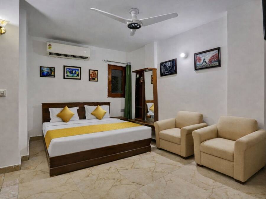 A hotel room with a bed, two armchairs, a ceiling fan, and wall-mounted air conditioning.
